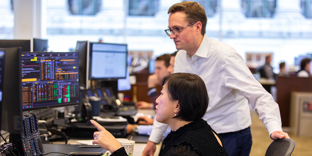 Two professionals looking at monitors at a trading desk